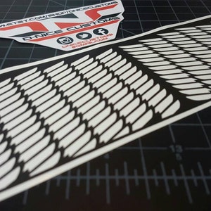May include: A white vinyl decal with a pattern of overlapping feathers on a black background. The decal is designed to be applied to a surface, such as a car or a laptop.