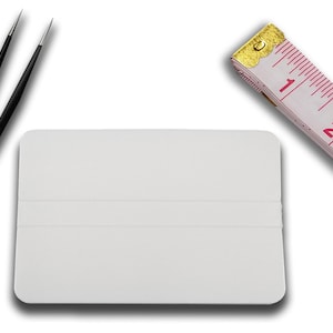 May include: A white rectangular scraper with two black lines, a pair of black tweezers, and a white tape measure with pink markings and the text "79inch".