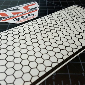 May include: A white sticker with a black honeycomb pattern. The sticker has a black border.