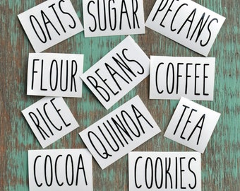 May include: White rectangular labels with black text for various pantry items, including oats, sugar, pecans, flour, beans, coffee, rice, quinoa, tea, cocoa, and cookies.
