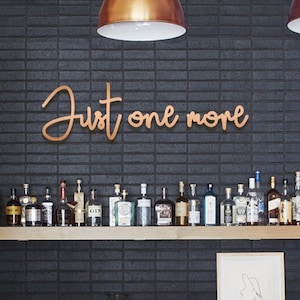May include: A black brick wall with a copper sign that reads "Just one more". There are copper light fixtures above the sign and a shelf with bottles of spirits below the sign.