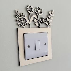 May include: A white light switch with a decorative wooden frame featuring a cutout design of flowers and leaves.