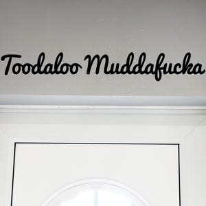 May include: A white door with a black cursive sign above it that reads "Toodaloo Muddafucha".