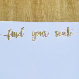 May include: Gold glitter letters spelling "find your seat" on a white background.