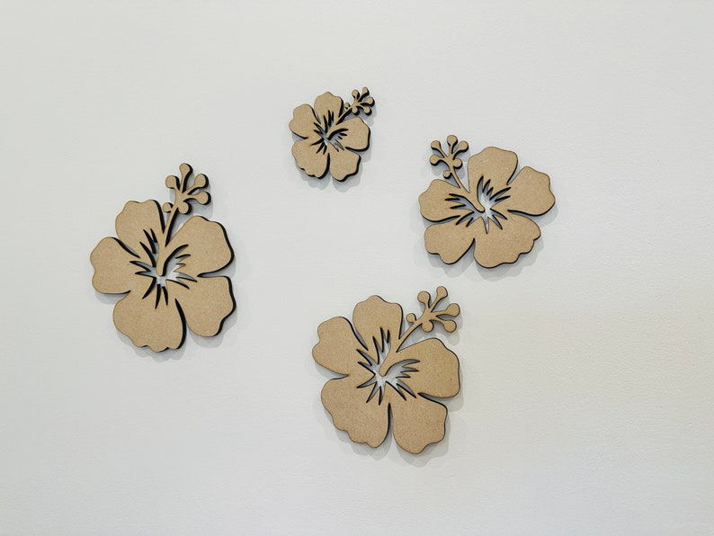 Peut inclure: Quatre fleurs d'hibiscus d&eacute;coup&eacute;es en bois brun sur un fond blanc.
