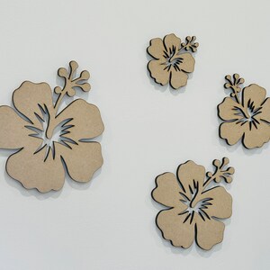 Peut inclure: Quatre fleurs d'hibiscus d&eacute;coup&eacute;es en bois brun de diff&eacute;rentes tailles. Les fleurs sont sur un fond blanc.
