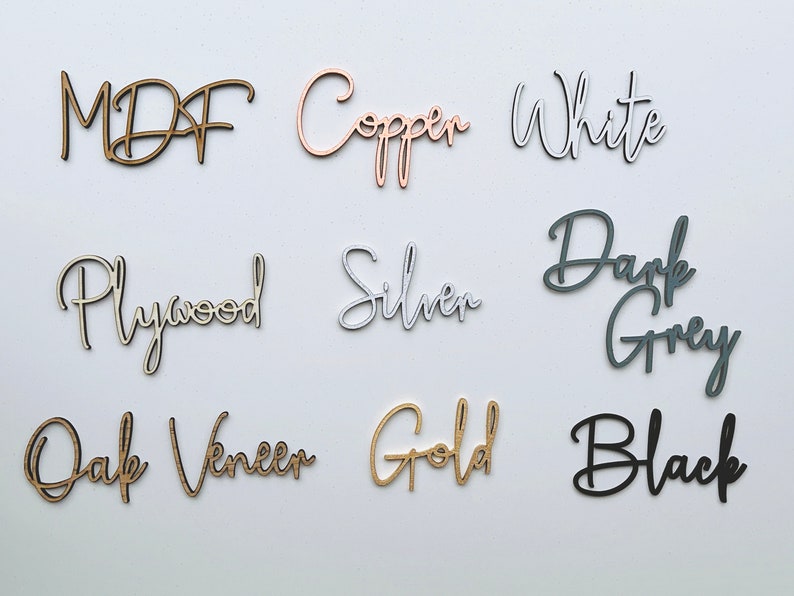 Peut inclure: Un ensemble de neuf mots d&eacute;coup&eacute;s au laser dispos&eacute;s en grille. Les mots sont MDF, Copper, White, Plywood, Silver, Dark Grey, Oak Veneer, Gold et Black. Chaque mot est pr&eacute;sent&eacute; dans un style de police script ou bloc avec des finitions uniques.