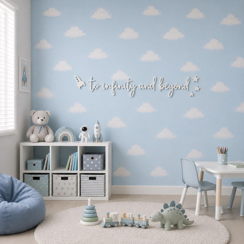 Peut inclure: Une enseigne murale blanche avec le texte en cursive to infinity and beyond, accompagn&eacute;e d'une petite fus&eacute;e et d'&eacute;toiles. L'enseigne est fix&eacute;e sur un mur bleu clair d&eacute;cor&eacute; d'un motif r&eacute;p&eacute;titif de nuages blancs.