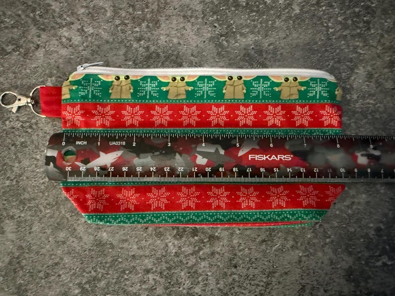 Puede incluir: Estuche rectangular con cierre de cremallera, con un dise&ntilde;o festivo. El estuche mide aproximadamente 20 cm de largo y tiene un patr&oacute;n rojo y verde con motivos de copos de nieve y personajes. Se adjunta un cierre plateado.