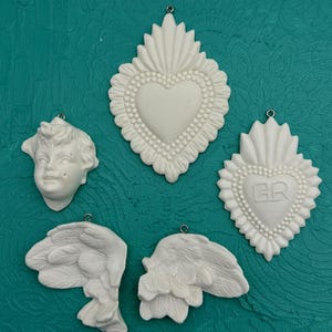 May include: Five white ceramic ornaments, including two sets of angel wings, a cherub face, and two heart-shaped ornaments with beaded borders. One heart has the initials "GR" embossed on it.