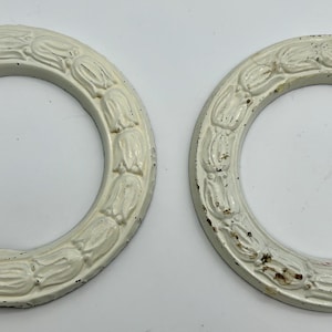 May include: Two off-white, circular decorative rings with a floral pattern around the edge. The rings have a distressed finish, with visible wear and tear. The background is a plain white surface.