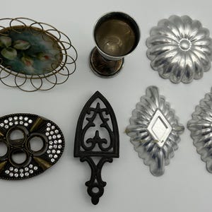 May include: Assortment of vintage kitchenware items, including a metal cake mold, a cast iron trivet, a small metal cup, a decorative metal dish with a floral design, and two metal molds with a diamond pattern.