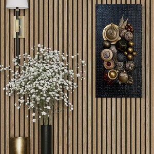 May include: An artistic wall decor piece featuring an arrangement of metallic and textured elements in gold, bronze, and black hues. The composition includes spheres, discs, and decorative accents on a dark background. A vase with white flowers and a lamp are also visible.
