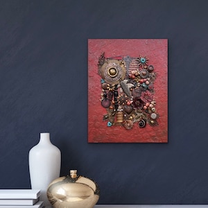Peut inclure: Une toile texturée rouge avec un collage de médias mixtes de perles dorées, brunes et rouges, de métal et d'autres éléments décoratifs. Le collage a la forme d'une fleur.