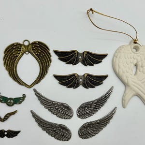 May include: Assortment of metal and ceramic angel wing charms in various sizes and finishes. The charms are in gold, silver, black, and white. Some charms have a peace sign design.