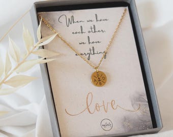 May include: A gold necklace with a round pendant featuring an anchor and the letters "P A D B". The necklace is in a grey box with a card that reads "When we have each other, we have everything love".