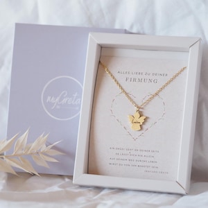 Könnte beinhalten: Eine weiße Geschenkbox mit einer goldenen Engelkette darin. Die Kette hat einen kleinen Engelanhänger mit dem Namen "Luisa" darauf. Die Box enthält eine Karte mit dem Text "Alles Liebe zu deiner Firmung" und einem Zitat über einen Engel, der über dich wacht.
