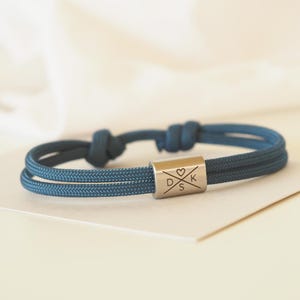 Könnte beinhalten: Ein blaues, doppelfädigiges Seil-Armband mit einem silbernen Anhänger mit den Initialen "D S K" und einem Herzsymbol.