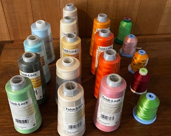 May include: A collection of 15 spools of thread in various colors, including green, pink, red, orange, beige, and blue. The spools are labeled "Toldi-Lock" and have different numbers and descriptions.