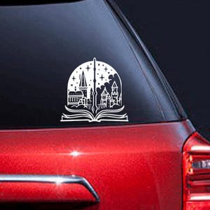 May include: White vinyl sticker of a book with a wand splitting it in half. The book is open and the wand is pointing up. The book has a castle silhouette inside. The sticker is on a red car.