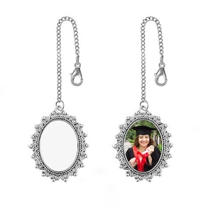 May include: Silver oval picture frame with a chain, the frame has a decorative design and is hanging from the chain. The frame has a photo of a woman in a graduation cap and gown holding a diploma.