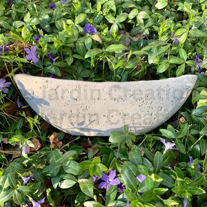 Op de afbeelding: Een grijze betonnen trogplanter met een ruwe textuur. De planter is halfrond en heeft de woorden "Garden Creations" in reli&euml;f op de voorkant.