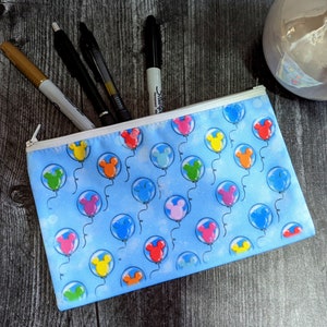 K&ouml;nnte beinhalten: Eine blaue Stiftebox mit Rei&szlig;verschluss. Die Box ist mit einem Muster aus bunten Ballons mit Mickey Mouse-Ohren verziert. Die Box ist mit Stiften und Markern gef&uuml;llt.