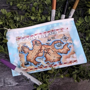 May include: A zippered pouch with a Neverland map design, featuring a compass rose and various locations. The pouch is light blue with a white zipper and contains several Sharpie markers in various colors. The pouch is approximately 9 inches long.