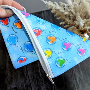 K&ouml;nnte beinhalten: Eine blaue Rei&szlig;verschlusstasche mit einem Muster aus bunten Mickey Mouse-Ballons. Die Tasche ist aus weichem Stoff gefertigt.