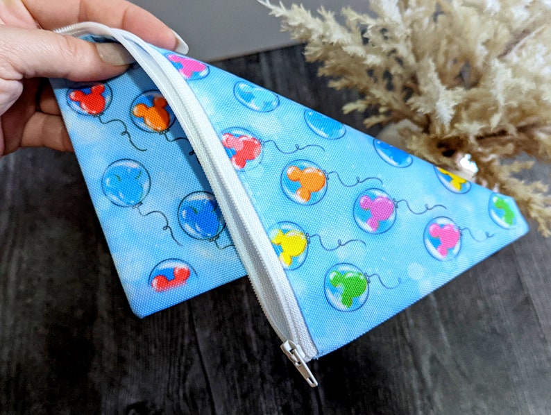 K&ouml;nnte beinhalten: Eine blaue Rei&szlig;verschlusstasche mit einem Muster aus bunten Mickey Mouse-Ballons. Die Tasche ist aus weichem Stoff gefertigt.