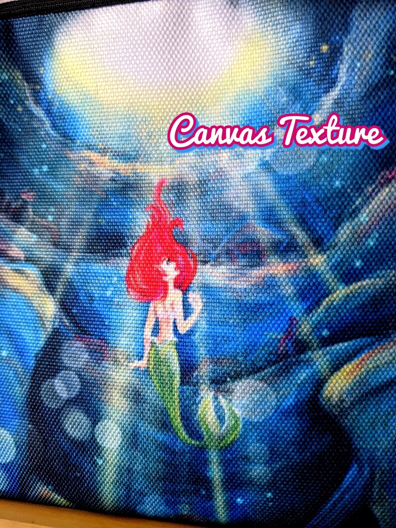 K&ouml;nnte beinhalten: Eine Canvas-Tragetasche mit einem aufgedruckten Bild von Arielle, der kleinen Meerjungfrau, die im Meer schwimmt. Das Bild hat ein blaues, gr&uuml;nes und rotes Farbschema. Der Text "Canvas Texture" ist auf die Tasche gedruckt.