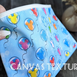 K&ouml;nnte beinhalten: Eine blaue Canvas-Rei&szlig;verschlusstasche mit einem wei&szlig;en Rei&szlig;verschluss. Die Tasche hat ein sich wiederholendes Muster aus bunten Luftballons mit Mickey-Maus-Ohren. Der Text "CANVAS TEXTURE" ist auf der Unterseite der Tasche aufgedruckt.