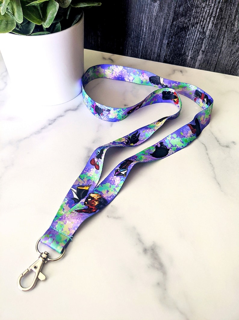 K&ouml;nnte beinhalten: Ein lilafarbenes Lanyard mit einem bunten Spr&uuml;hfarben-Design und Comicfiguren. Das Lanyard hat einen silbernen Metallclip.