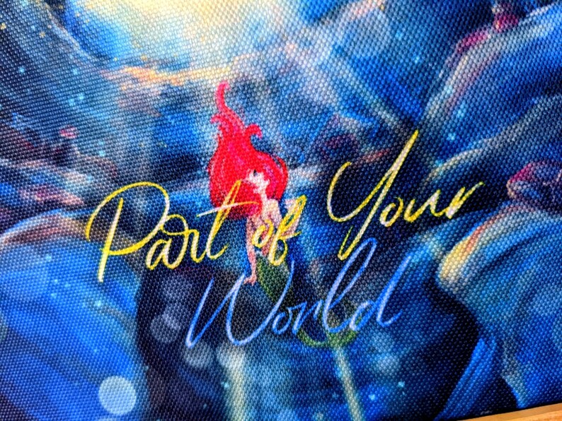 K&ouml;nnte beinhalten: Ein blaues und goldenes Leinwandbild mit einer Meerjungfrau mit roten Haaren und einem gelben Schwanz. Der Text "Part of Your World" ist in goldener Kursivschrift geschrieben.