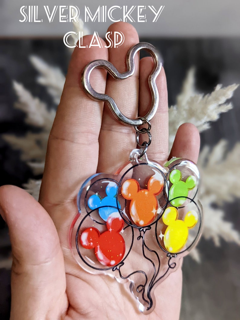 Puede incluir: Un llavero de Mickey Mouse plateado con un dije de cinco cabezas de Mickey Mouse de colores dentro de globos transparentes.