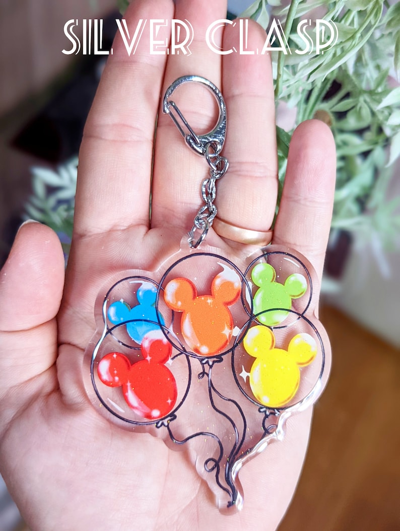 Puede incluir: Un llavero de plata con un dije que presenta cinco globos de Mickey Mouse de colores. Los globos son rojo, naranja, amarillo, verde y azul.