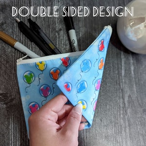 K&ouml;nnte beinhalten: Eine blaue Rei&szlig;verschlusstasche mit einem Mickey Mouse Ballon-Druck. Die Tasche ist ge&ouml;ffnet und zeigt das Innere, das ebenfalls mit Mickey Mouse Ballons bedruckt ist. Der Text "DOUBLE SIDED DESIGN" ist oben im Bild sichtbar.
