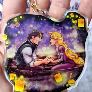 May include: A clear, cat-shaped keychain featuring a romantic scene with a man and woman in a boat, surrounded by floating lanterns. The artwork has a glittery effect and a gold-colored chain.