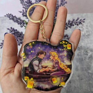 May include: A clear acrylic keychain featuring a romantic scene with a man and woman in a boat, surrounded by floating lanterns. The keychain has a gold-colored keyring and chain.