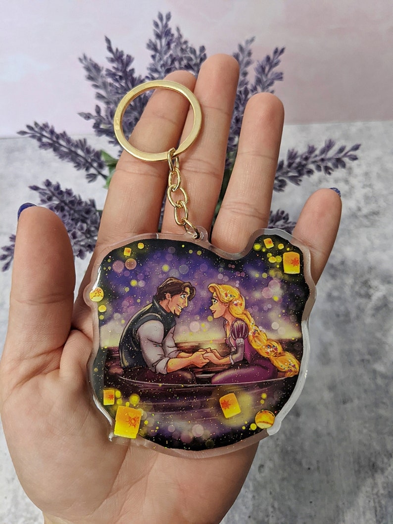 May include: A clear acrylic keychain featuring a romantic scene with a man and woman in a boat, surrounded by floating lanterns. The keychain has a gold-colored keyring and chain.