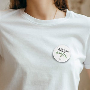 May include: White button with black text that reads "I'm the bride, pour me a martini". The button has a green martini glass graphic.