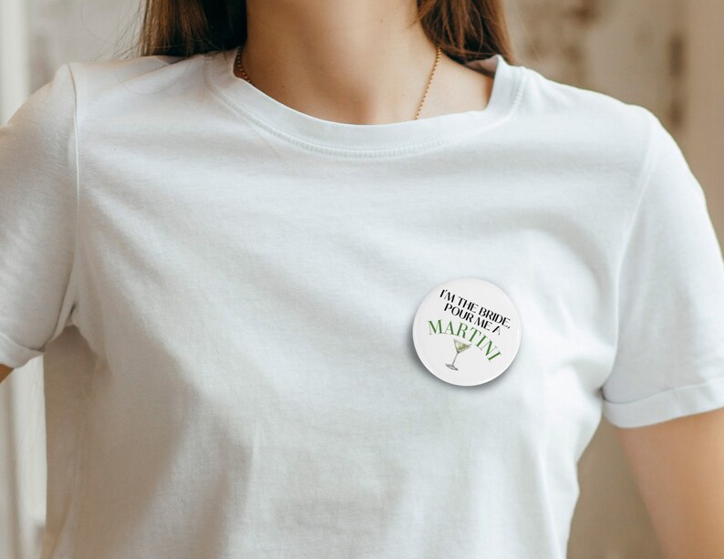 May include: White button with black text that reads "I'm the bride, pour me a martini". The button has a green martini glass graphic.