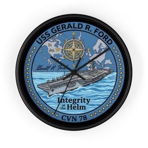 Puede incluir: Un reloj de pared redondo negro con el portaaviones USS Gerald R. Ford. La esfera del reloj es azul con una rosa de los vientos, un mapa y el texto "Integrity at the Helm". Las manecillas son negras.