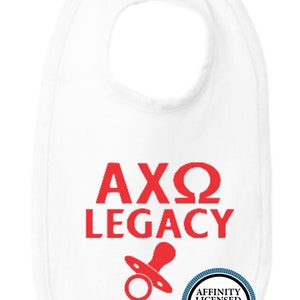 May include: White baby bib with red text reading "AXΩ LEGACY" and a red pacifier graphic. A circular logo with the text "AFFINITY LICENSED PRODUCT" is on the bottom right. The bib is designed for infants.