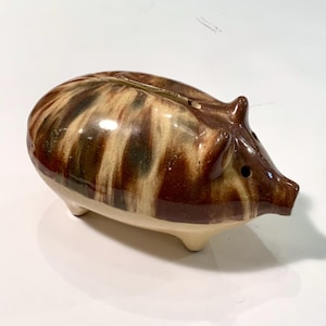May include: A brown and white ceramic piggy bank with a swirl pattern. The piggy bank has a slot on the top for coins and a small hole on the side for removing coins.