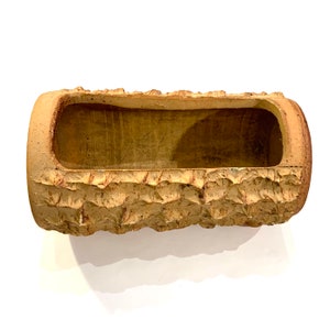 May include: A brown ceramic planter shaped like a log with a rough, textured surface.