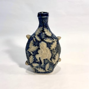 May include: A blue and white ceramic bottle with a relief design of a figure playing a musical instrument surrounded by foliage.
