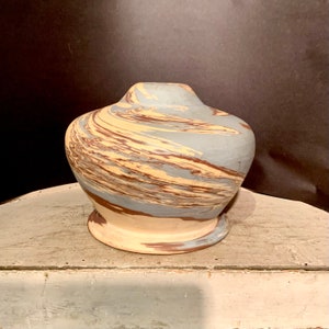 May include: A ceramic vase with a marbled design in shades of blue, brown, and cream. The vase has a rounded body and a flared base.