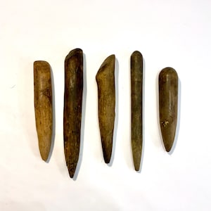 May include: Five handcrafted wooden tools of varying shapes and sizes, arranged against a white background. The tools are primarily shades of brown, with visible wood grain and natural imperfections, suggesting a rustic aesthetic.