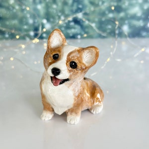 May include: A ceramic figurine of a corgi dog with brown and white fur. The dog is sitting with its tongue sticking out and has a happy expression.